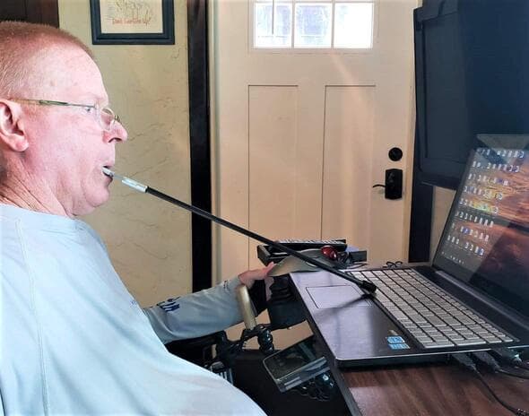 A man using a mouth stick to operate a laptop keyboard.